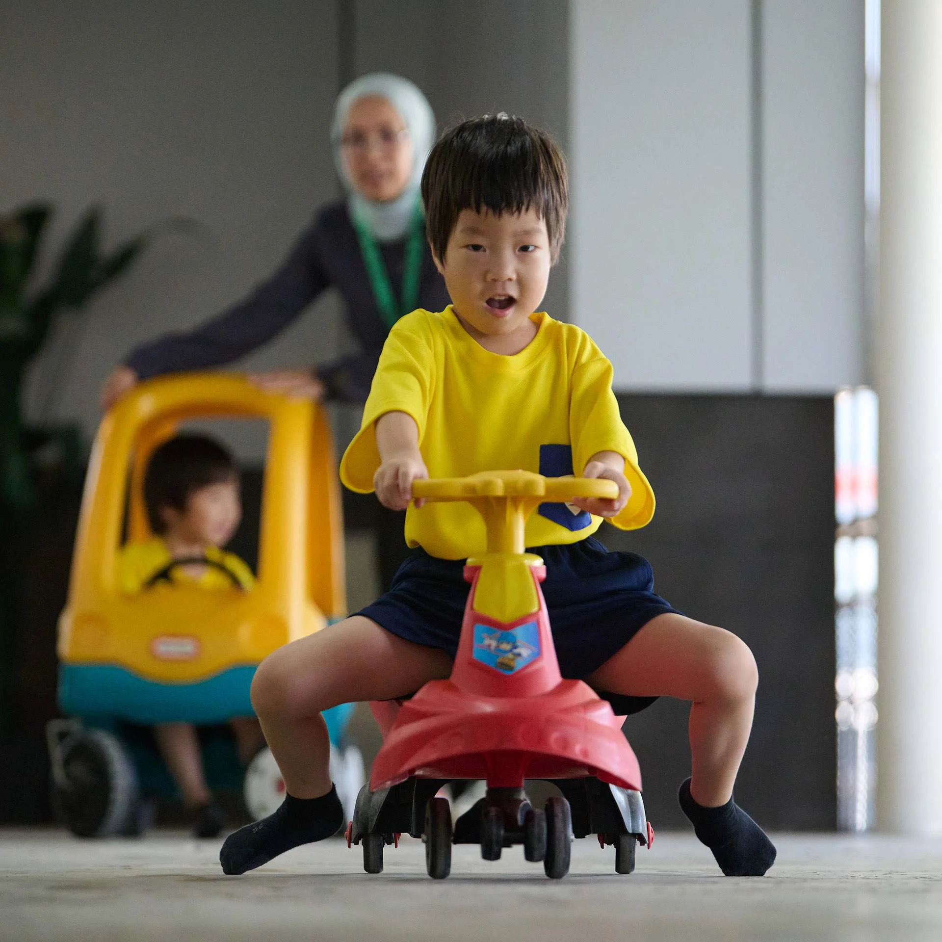 Kids driving a toy vehicle while being supervised by their teacher