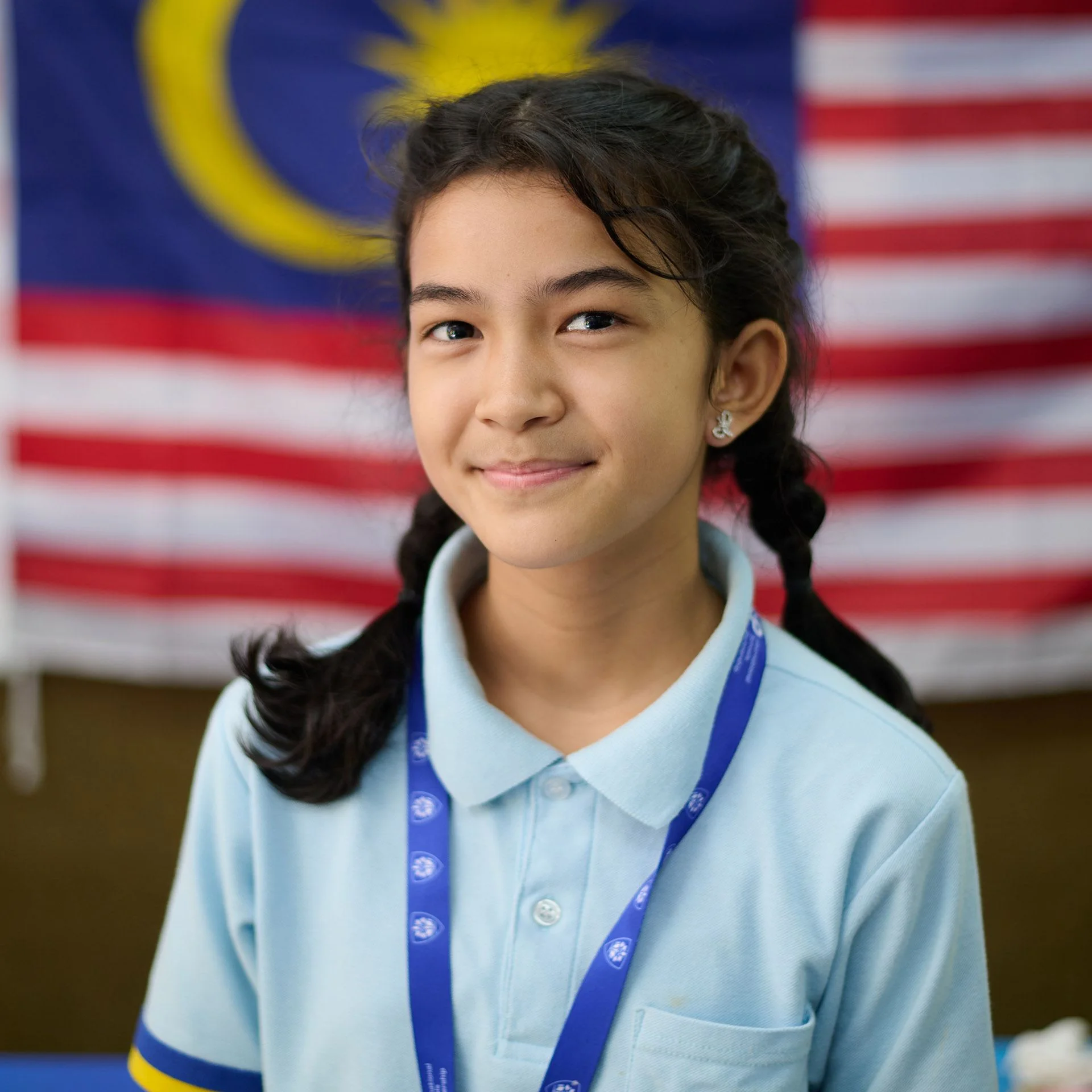 Primary school student smiling in front of a Malaysian flag